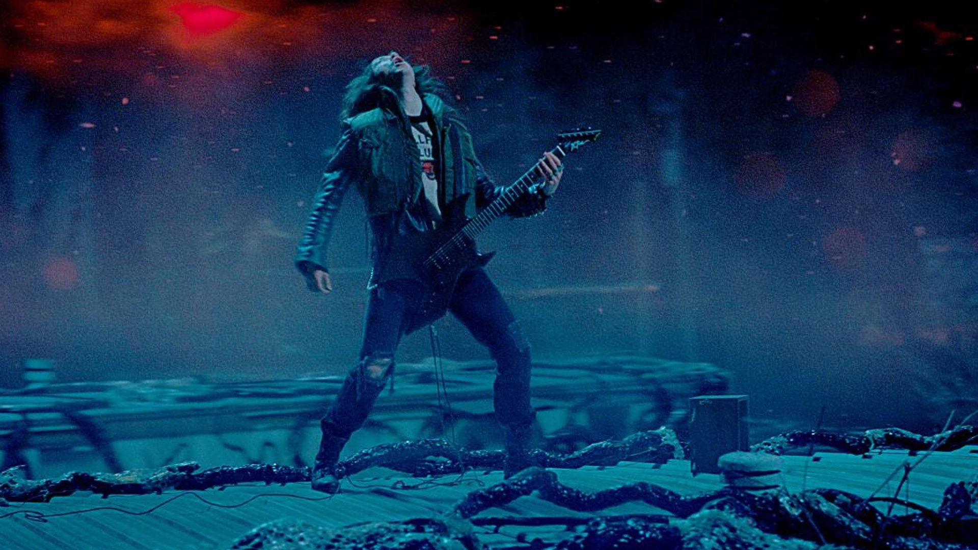 Guitarrista rockeando en escenario oscuro y fogoso.